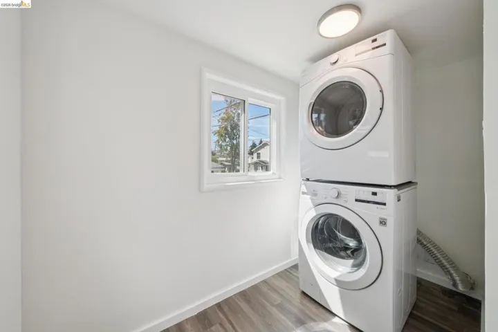 Laundry area featuring a stackable washer and dryer, wood-finish flooring, a window, and overhead lighting