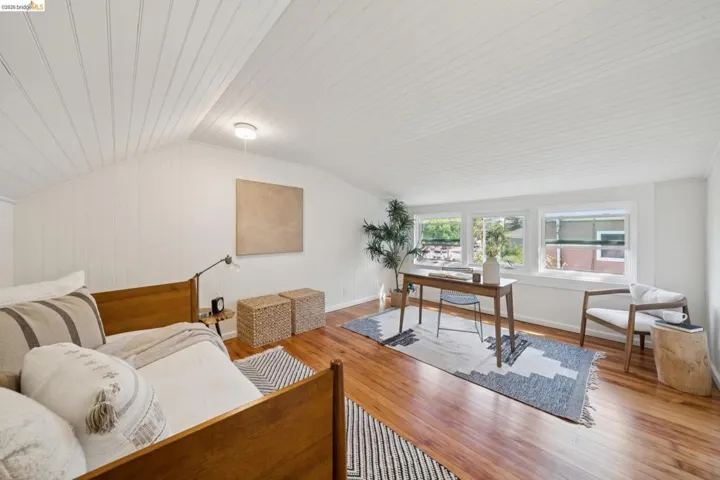 Vaulted ceiling with white paneling, wood-finish flooring, white paneled walls, and three windows with white trim