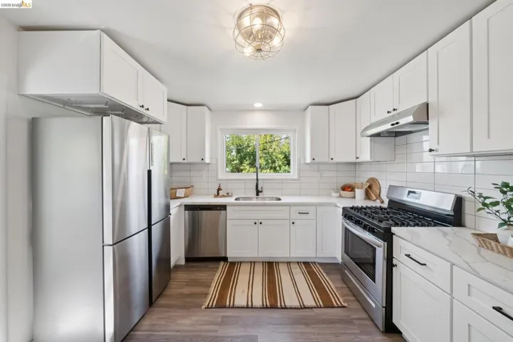 White shaker cabinetry, stainless steel appliances, wood-finish flooring, subway tile backsplash, and light-toned countertops