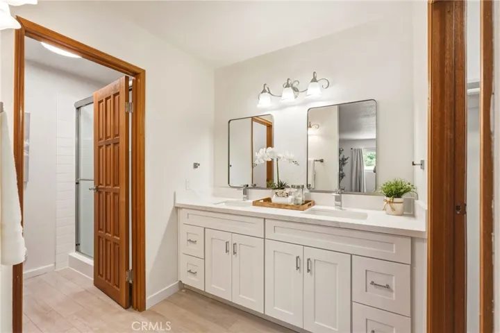 Fully updated bathroom with a dual-sink quartz vanity, rain shower with custom niche, private water closet, and walk-in closet