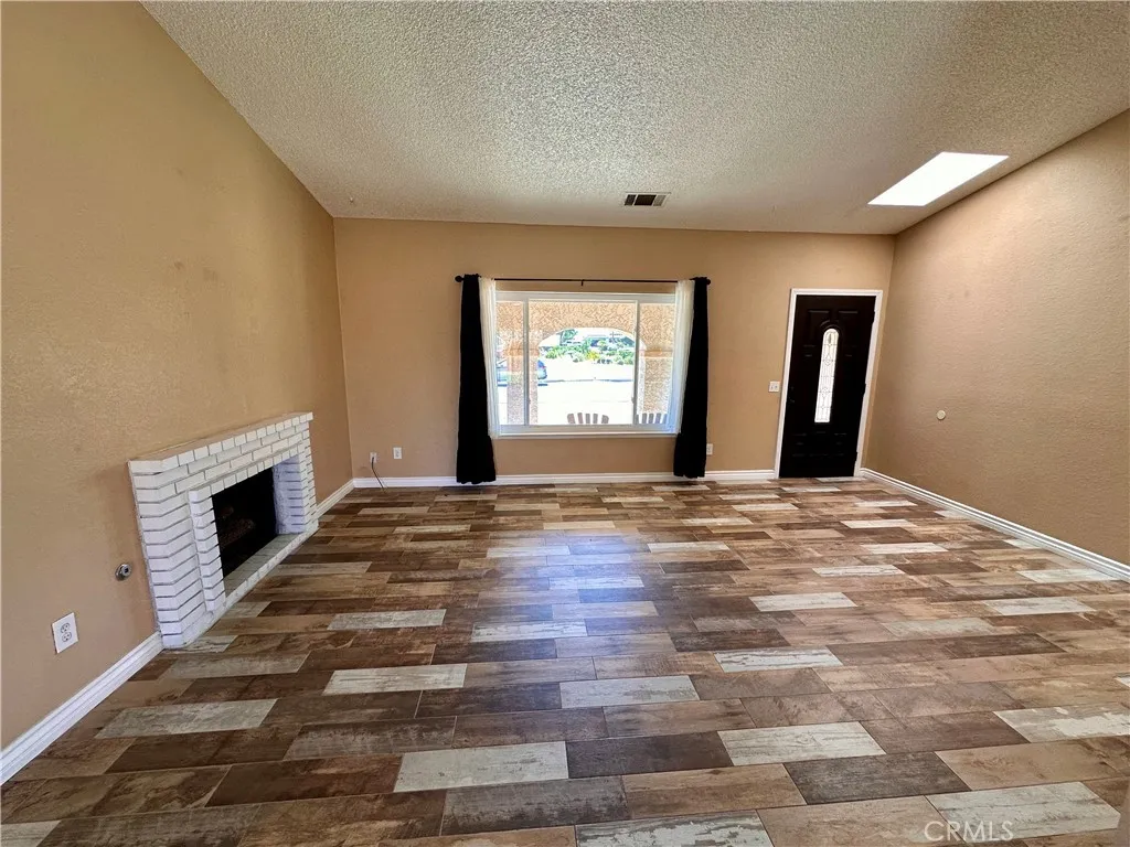 This spacious living room features vaulted ceilings, wood-look flooring, a white brick fireplace, and a large front-facing window that brings in abundant natural light. This spacious living room features vaulted ceilings, wood-look flooring, a white brick fireplace, and a large front-facing window that brings in abundant natural light.