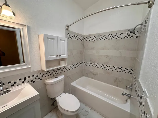 The bathroom features a tub-and-shower combination surrounded by large-format tile with decorative mosaic accents, along with a vanity and additional wall storage.