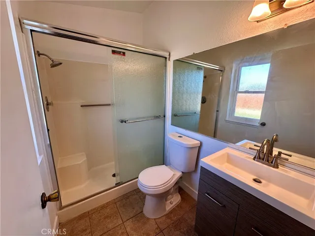 A second bathroom features a walk-in shower with sliding glass doors, a contemporary vanity, large mirror, and a window for natural light.
