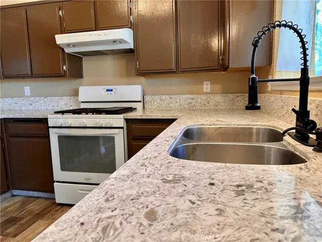 A closer look highlights the Quartz countertops, double-basin stainless steel sink, high-arc faucet, gas range, and ample cabinet storage.