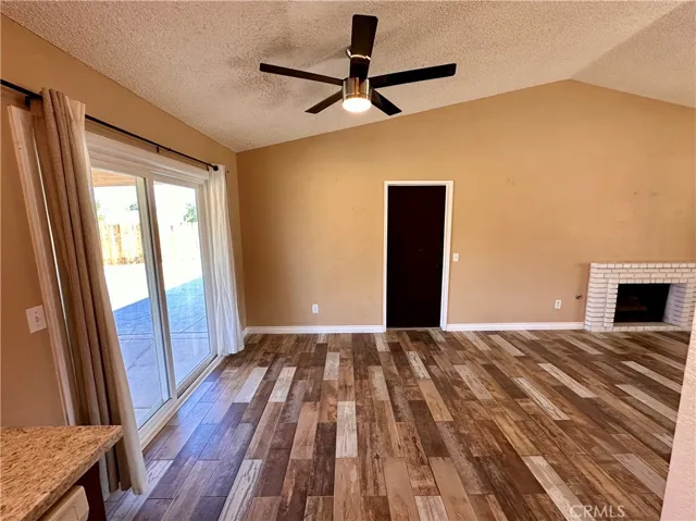 A spacious living area features wood-look flooring, a ceiling fan, fireplace, and sliding glass doors that provide easy access to the outdoor area.