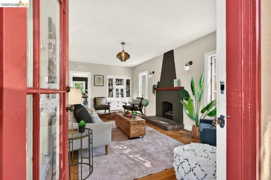 Red-painted French doors opening into a living space featuring wood-finish flooring, a contemporary fireplace with a dark mantel, built-in cabinetry, and a decorative ceiling light fixture Red-painted French doors opening into a living space featuring wood-finish flooring, a contemporary fireplace with a dark mantel, built-in cabinetry, and a decorative ceiling light fixture