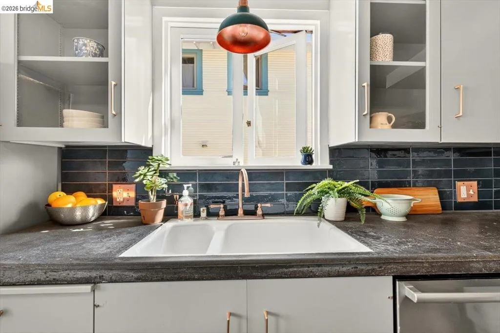 Double basin sink with a copper-finish faucet, dark subway tile backsplash, and light gray cabinetry with copper-finish hardware Double basin sink with a copper-finish faucet, dark subway tile backsplash, and light gray cabinetry with copper-finish hardware