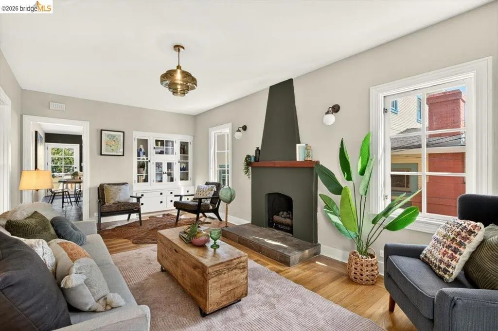 Living area featuring wood-finish flooring, a built-in display cabinet, a fireplace with a substantial hearth, and multiple windows Living area featuring wood-finish flooring, a built-in display cabinet, a fireplace with a substantial hearth, and multiple windows