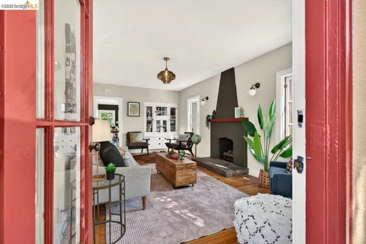 Red-painted French doors opening into a living space featuring wood-finish flooring, a contemporary fireplace with a dark mantel, built-in cabinetry, and a decorative ceiling light fixture
