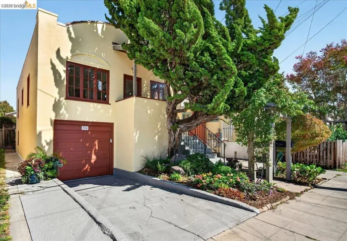 Stucco exterior with a terracotta garage door, integrated garage, concrete driveway, and established landscaping