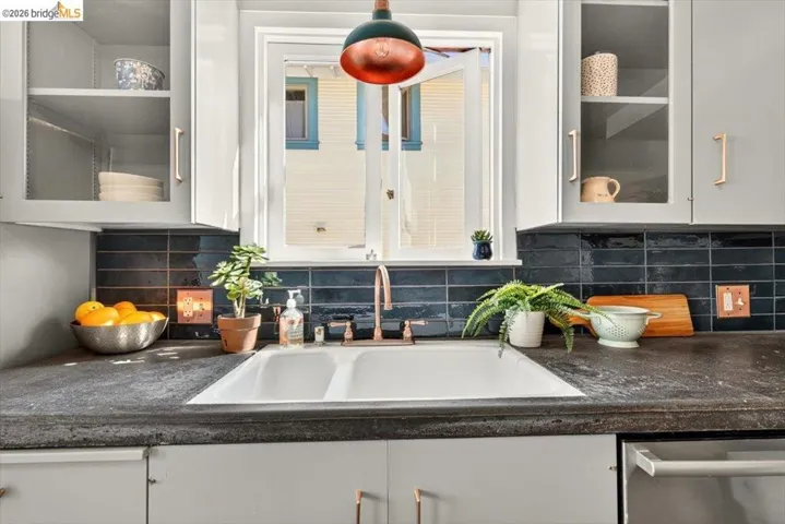 Double basin sink with a copper-finish faucet, dark subway tile backsplash, and light gray cabinetry with copper-finish hardware