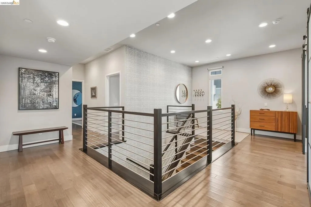 Upper-level landing featuring wood-finish flooring, recessed lighting, and a modern stair railing with dark wood and metal balusters