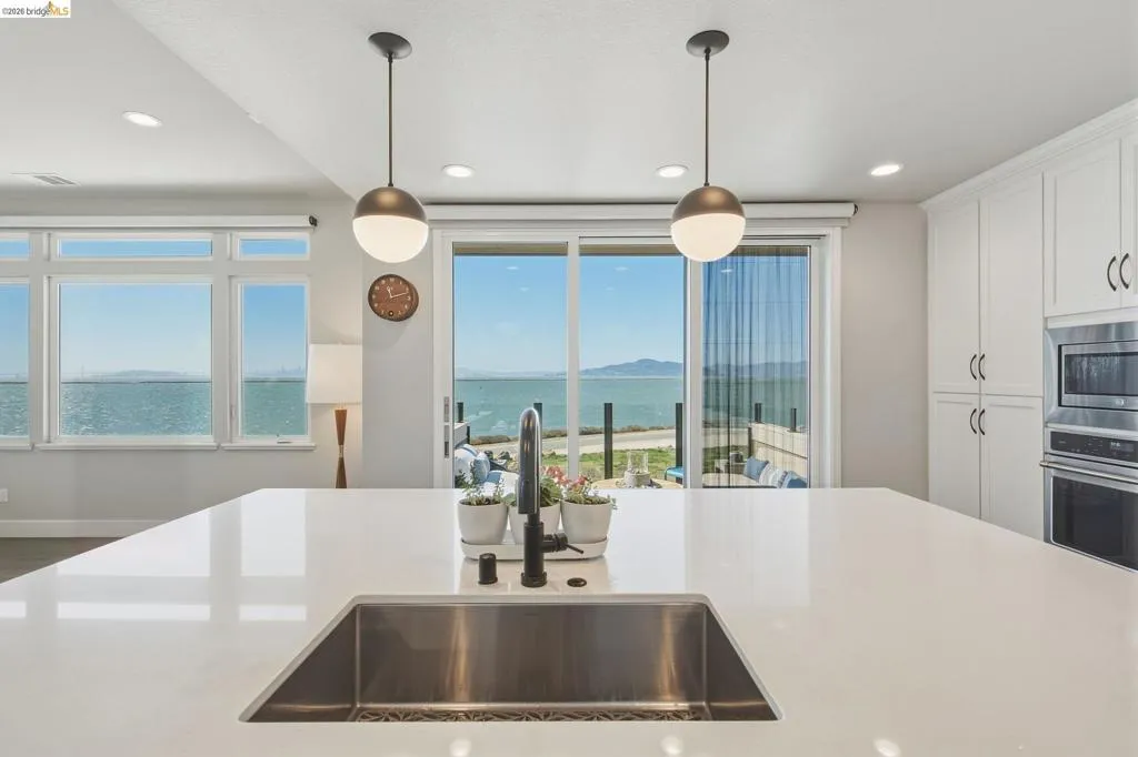 Expansive kitchen island with an undermount stainless steel sink, white cabinetry, integrated stainless steel appliances, and a sliding glass door to an outdoor area