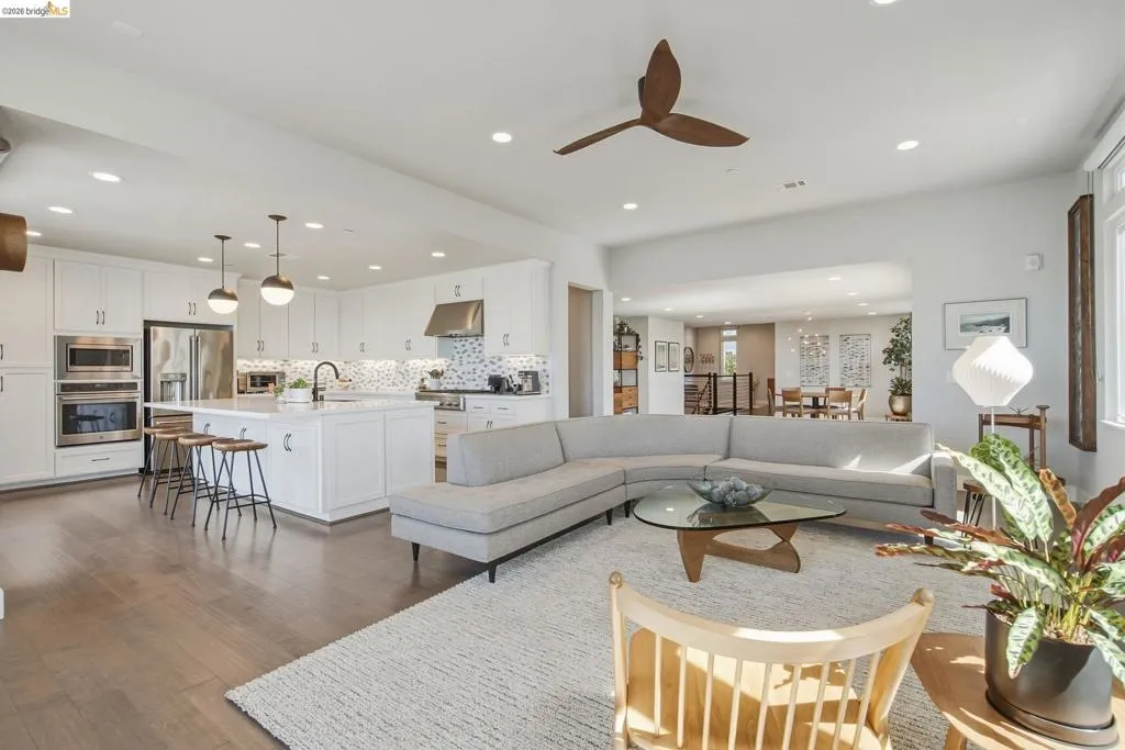 Open-concept living space featuring wood-finish flooring, recessed lighting, a modern ceiling fan, white cabinetry with stainless steel appliances, and an island with pendant lighting
