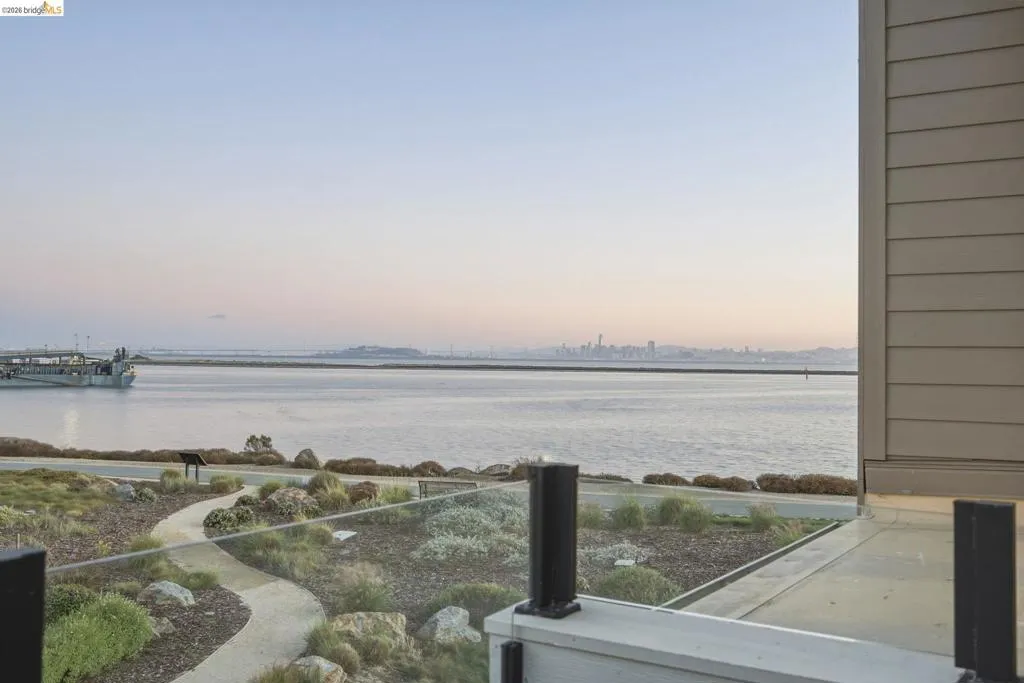 Glass balcony railing overlooking a waterfront setting with a distant city skyline