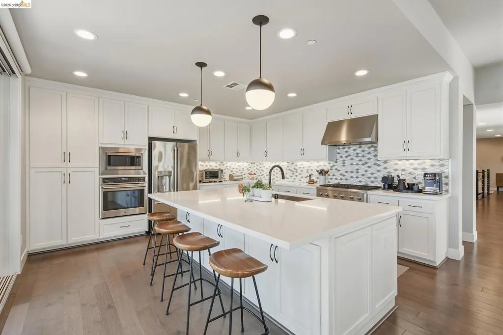 Kitchen featuring extensive white cabinetry, a large center island with counter seating, stainless steel appliances, a tile backsplash, and wood-finish flooring