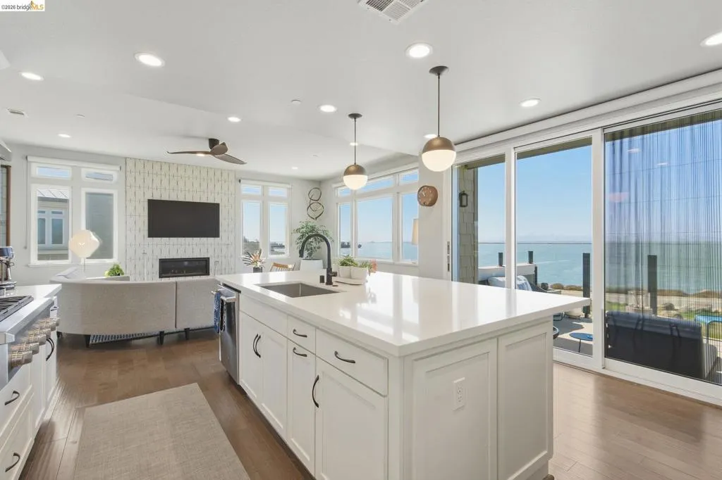 Open-concept living space with wood-finish flooring, a kitchen island with integrated sink, sliding glass doors, and recessed lighting