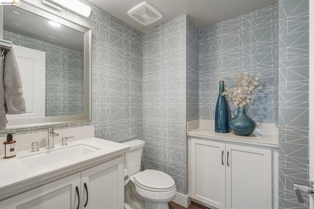 Built-in white cabinetry, integrated sink, wall-mounted mirror, and geometric pattern wall covering