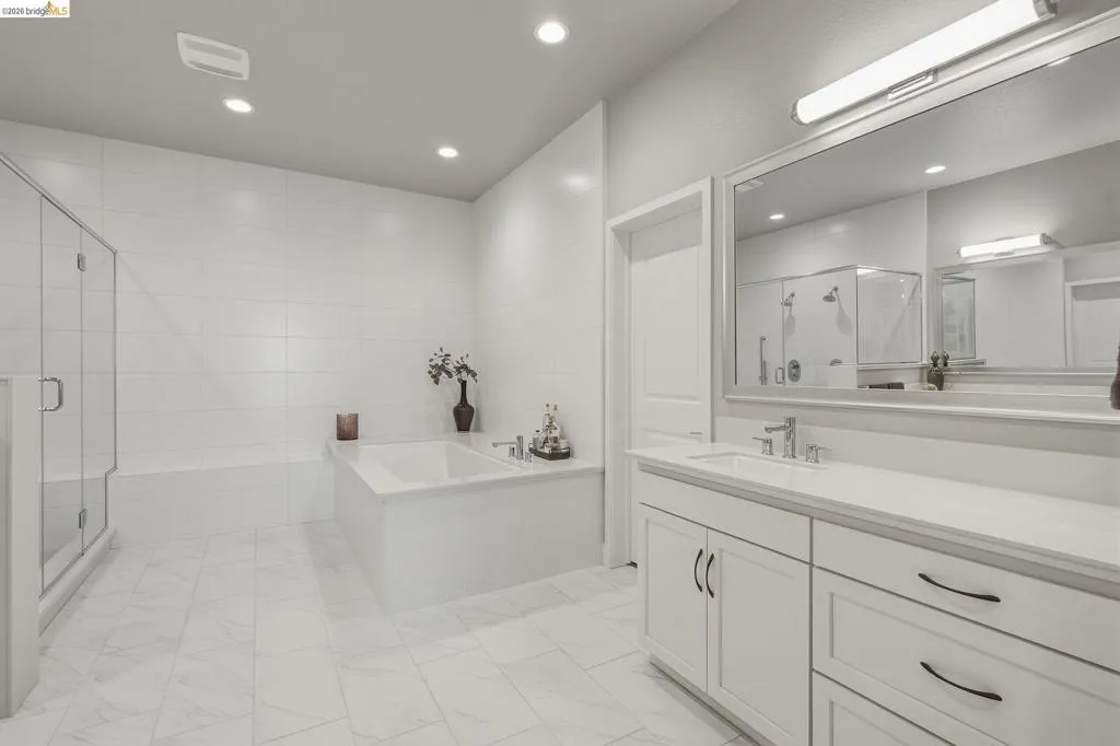 Spacious bathroom featuring a built-in soaking tub, glass-enclosed shower, dual-sink vanity with white cabinetry, and recessed lighting
