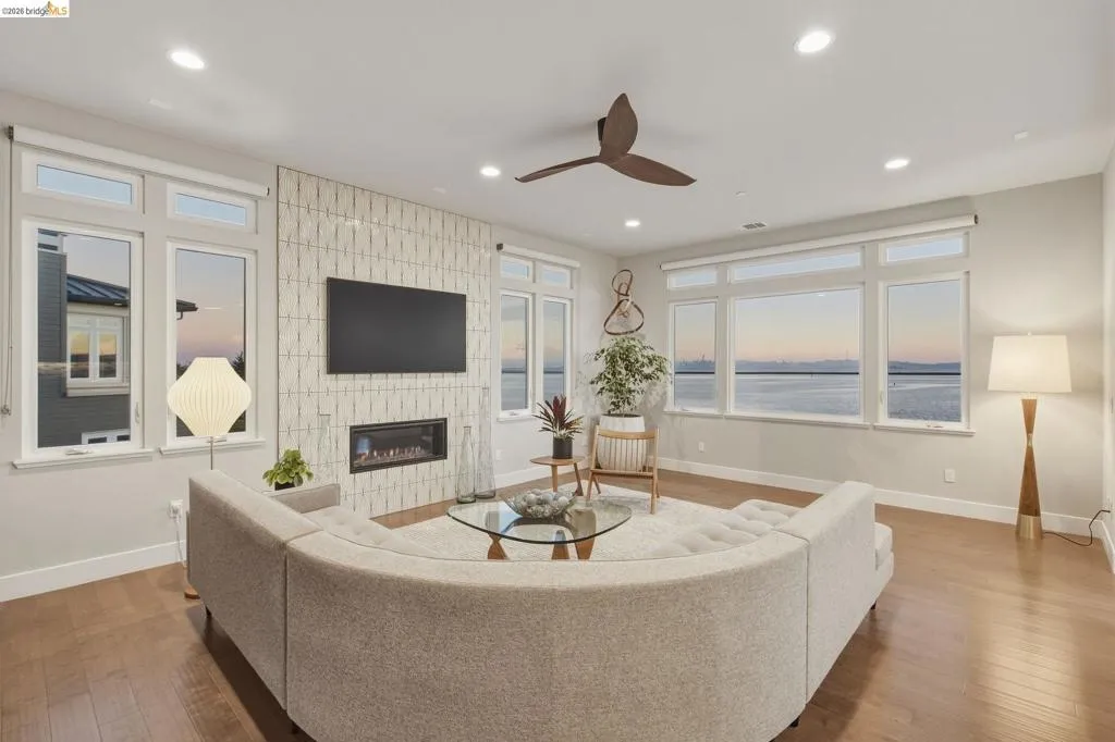 Spacious living area featuring large windows, wood-finish flooring, a contemporary fireplace, recessed lighting, and a ceiling fan