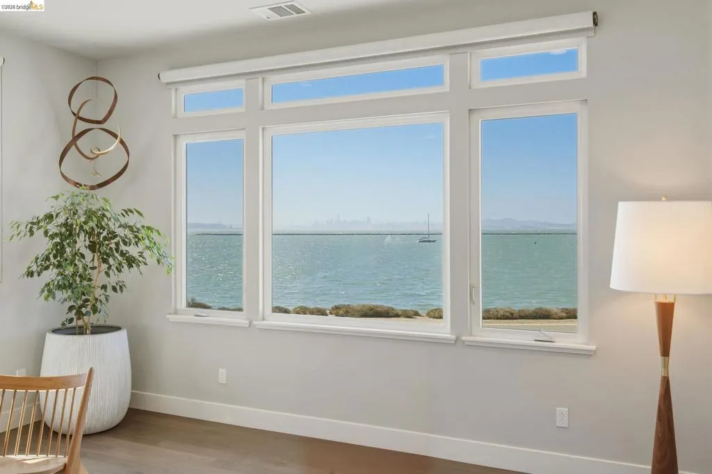 Expansive multi-pane windows with transoms, water frontage, light gray wall finish, and wood-finish flooring