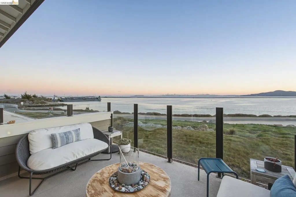 Spacious balcony featuring glass panel railing, concrete flooring, and water scenery