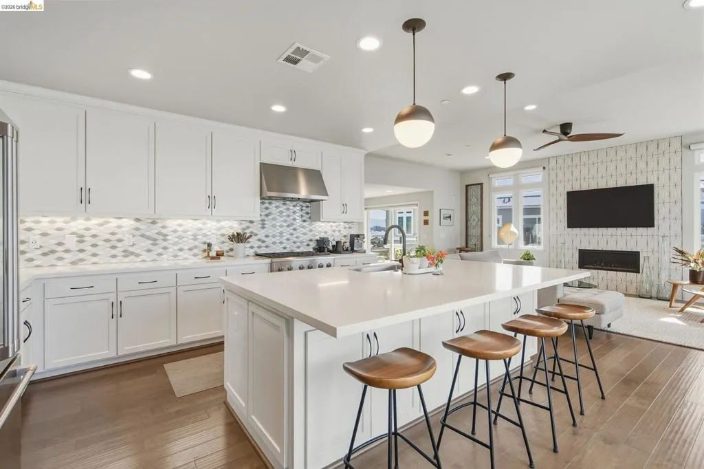 Modern kitchen featuring white cabinetry, a mosaic tile backsplash, stainless steel appliances, and a large waterfall-edge island with seating for multiple guests