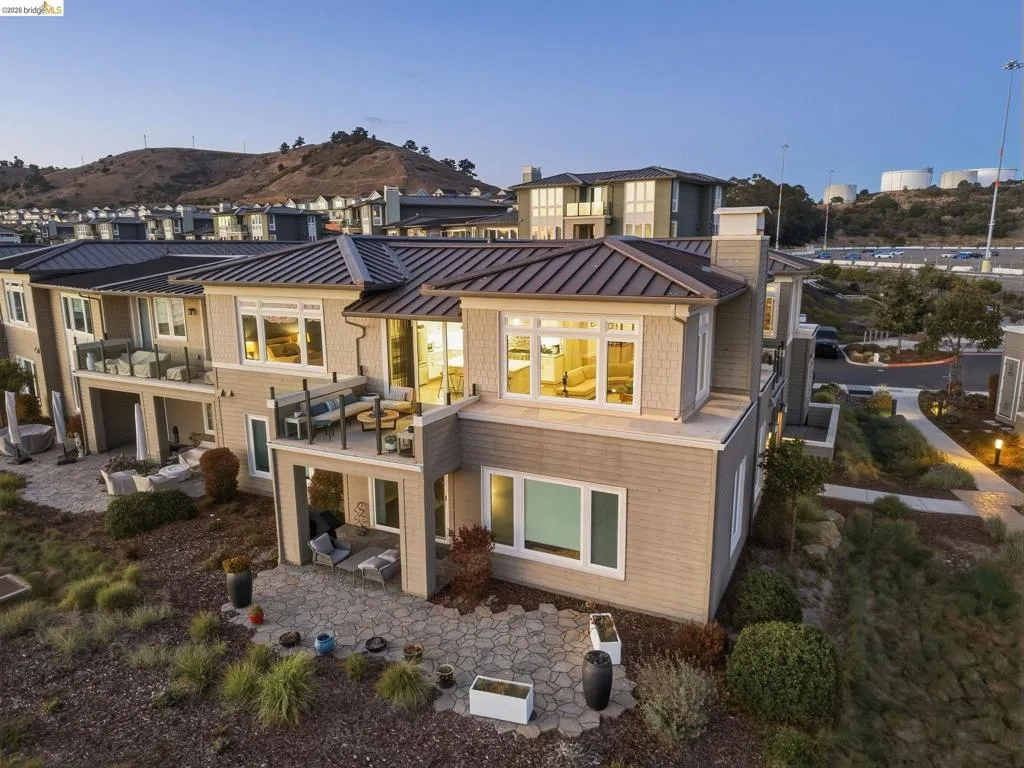 Terraced property with multiple patios, private balconies featuring glass railings, a stone patio, and a panel roof