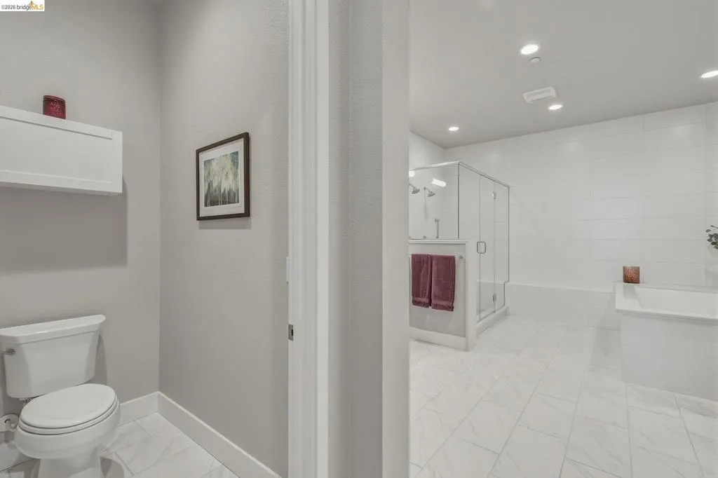 White tile flooring, built-in soaking tub, glass-enclosed shower, wall-mounted cabinetry, and recessed lighting