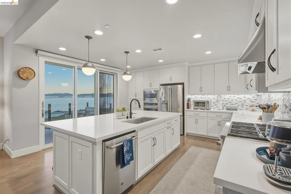Modern kitchen featuring white shaker cabinetry, a large waterfront-facing window, stainless steel appliances, white quartz countertops, and a center island with seating