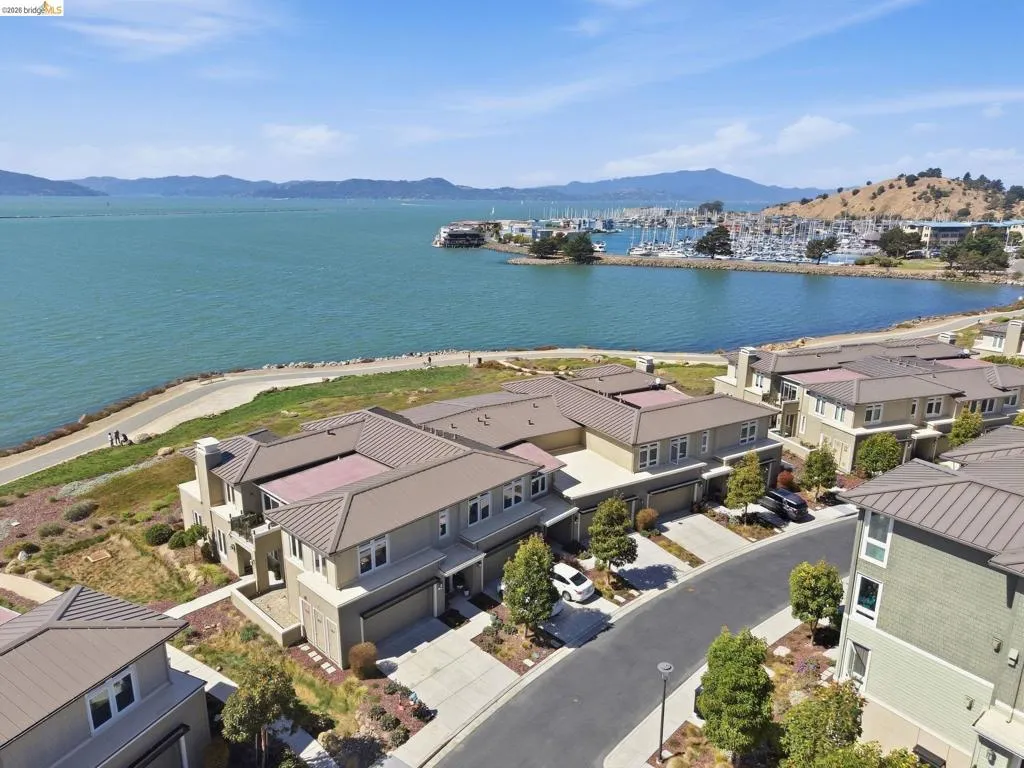Waterfront property featuring contemporary architecture, a paved residential street, integrated garages, and mature landscaping