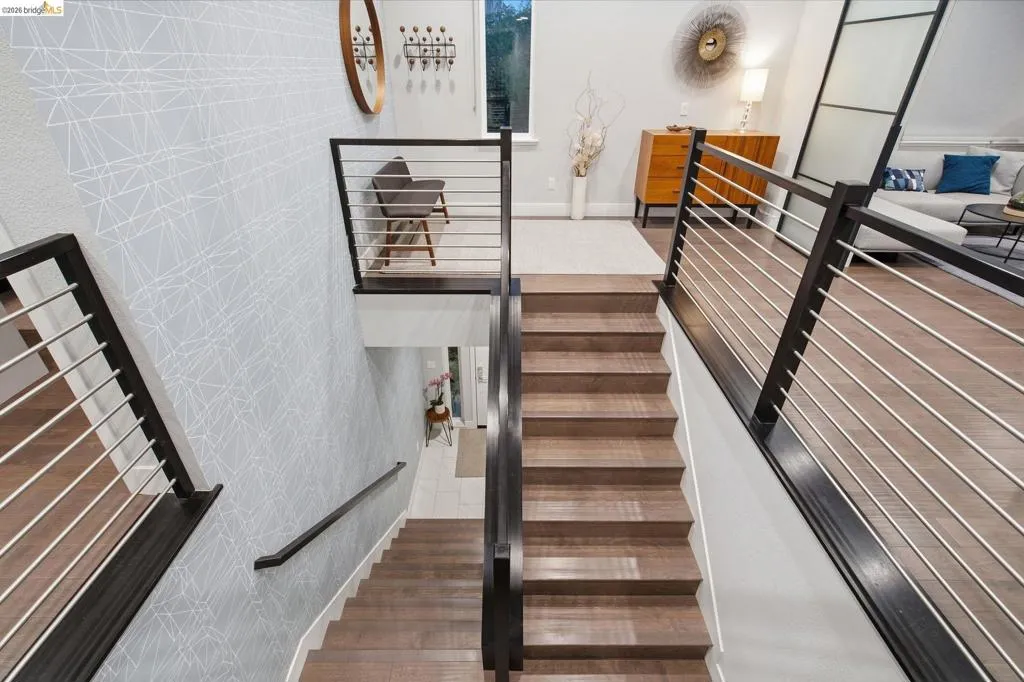 Hardwood staircases with cable railing, wood-finish flooring, and a patterned accent wall