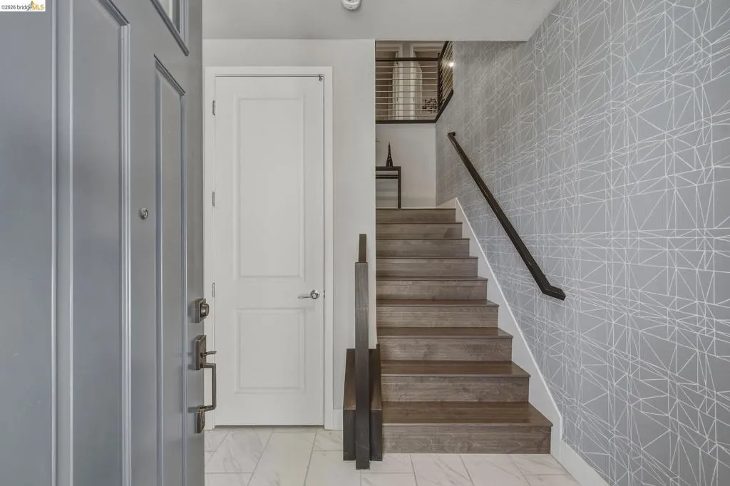 Entryway featuring a paneled door, wood-finish staircase, and patterned wall covering
