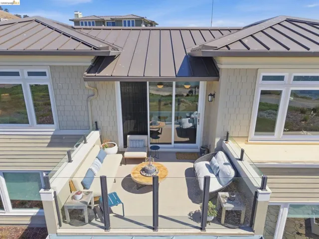 Private balcony featuring a glass railing, sliding door access, exterior wall sconce, and standing seam metal roof