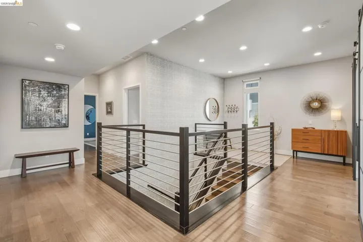Upper-level landing featuring wood-finish flooring, recessed lighting, and a modern stair railing with dark wood and metal balusters