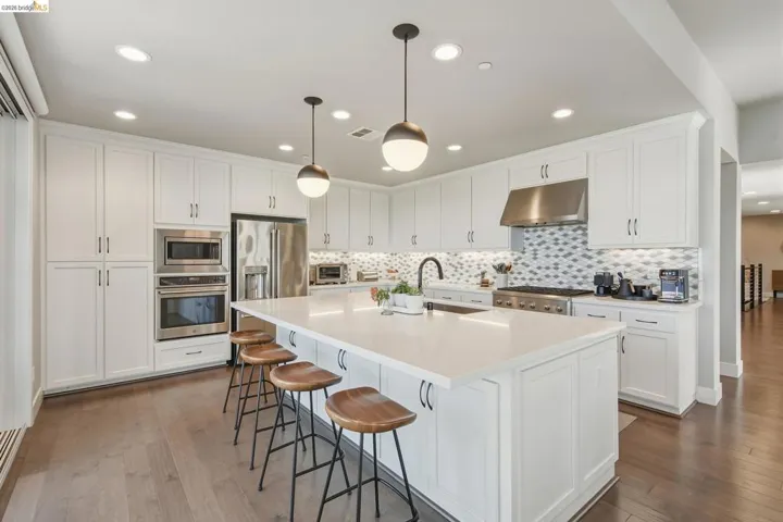 Kitchen featuring extensive white cabinetry, a large center island with counter seating, stainless steel appliances, a tile backsplash, and wood-finish flooring