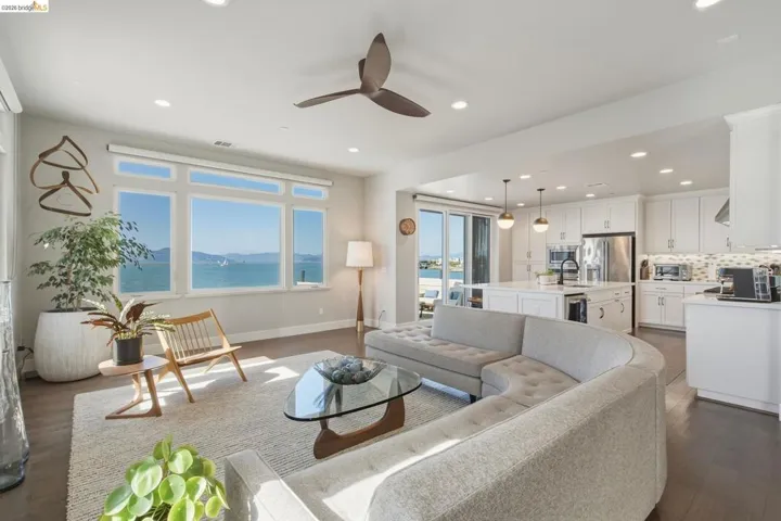 Open concept living area with expansive waterfront windows, recessed lighting, wood-finish flooring, and a kitchen featuring white cabinetry and a central island