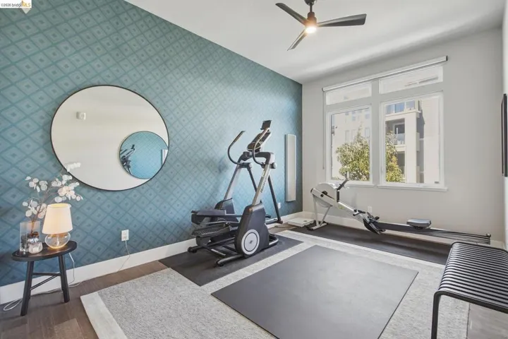 Accent wall with patterned wallpaper, large windows with roller blinds, and a ceiling fan