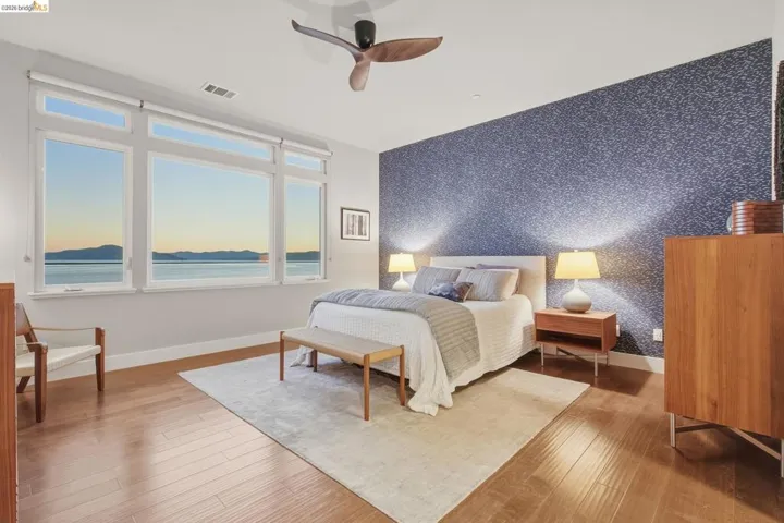 Expansive multi-pane window with water and mountain scenery, wood-finish flooring, accent wall with textured finish, ceiling fan, and recessed lighting