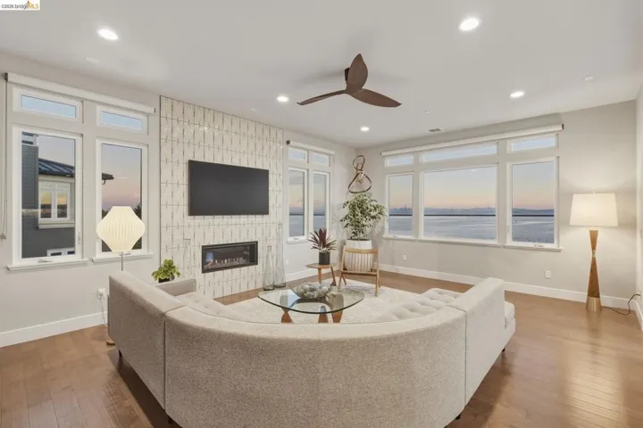 Spacious living area featuring large windows, wood-finish flooring, a contemporary fireplace, recessed lighting, and a ceiling fan