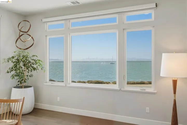 Expansive multi-pane windows with transoms, water frontage, light gray wall finish, and wood-finish flooring