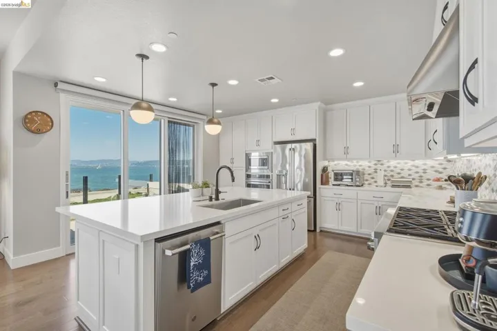 Modern kitchen featuring white cabinetry, stainless steel appliances, a center island with sink, pendant lighting, and wood-finish flooring