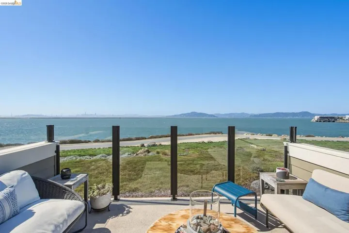 Outdoor patio featuring a glass railing system, concrete flooring, and a waterfront backdrop