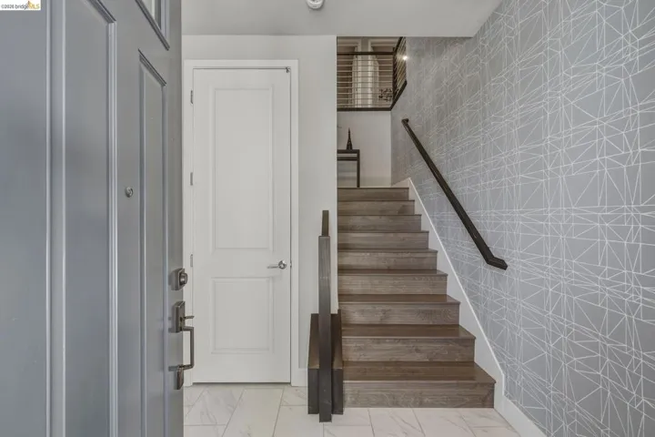 Entryway featuring a paneled door, wood-finish staircase, and patterned wall covering
