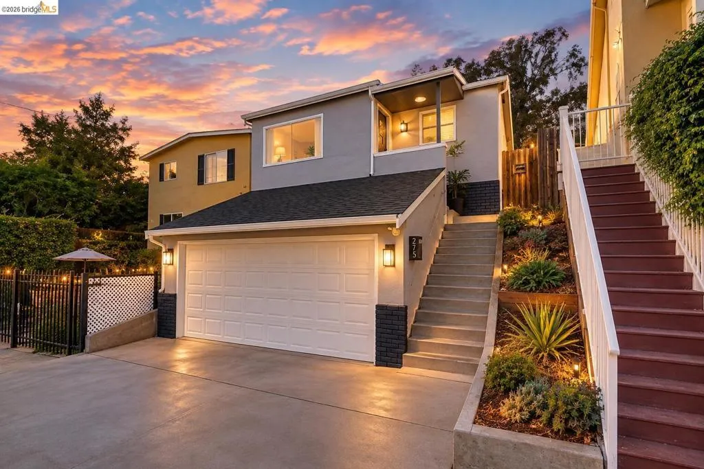 Multi-level property with an attached garage, landscaped terraced garden, concrete driveway, and an exterior staircase