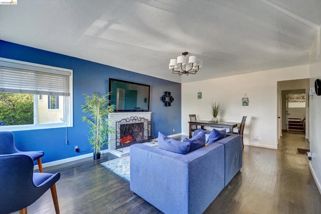 Living area featuring dark wood-finish flooring, a brick fireplace with an ornate screen, and a window with blinds