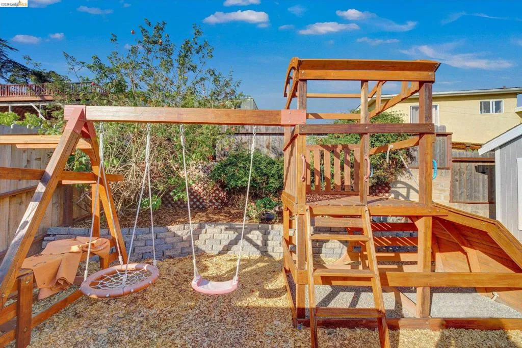 Outdoor play structure with a slide, swings, and an elevated platform, set on a wood chip surface