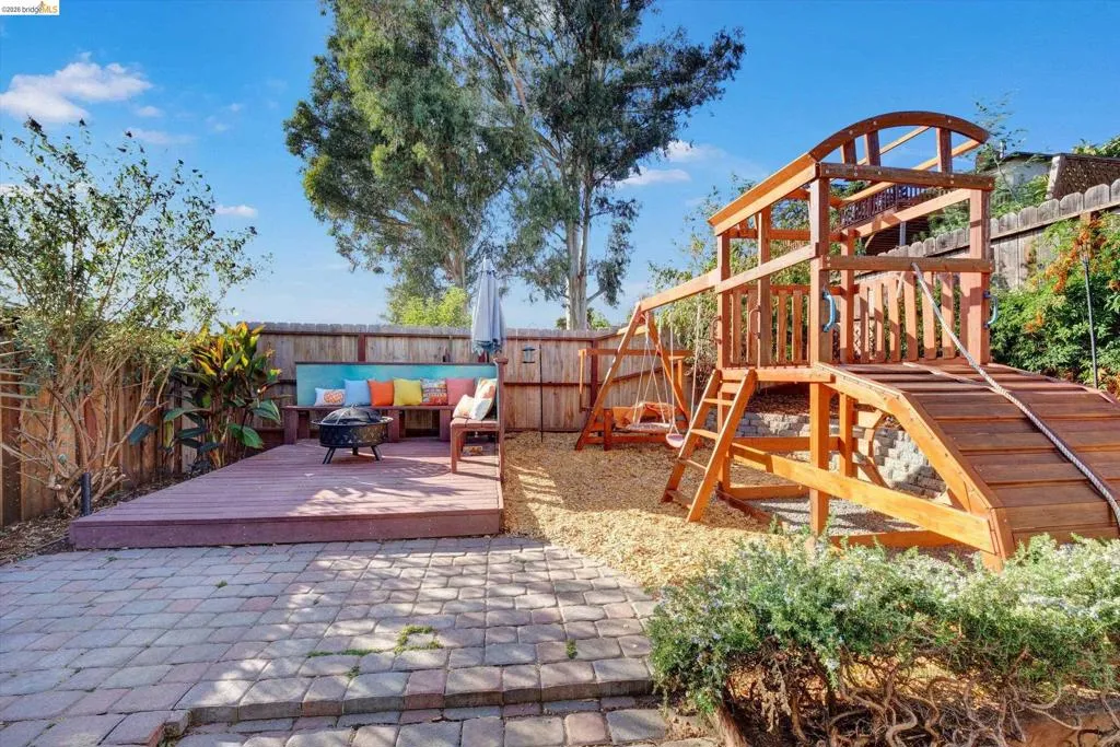 Paver patio, expansive wooden deck with built-in seating, privacy fencing, and a large wooden playset with swings and a slide