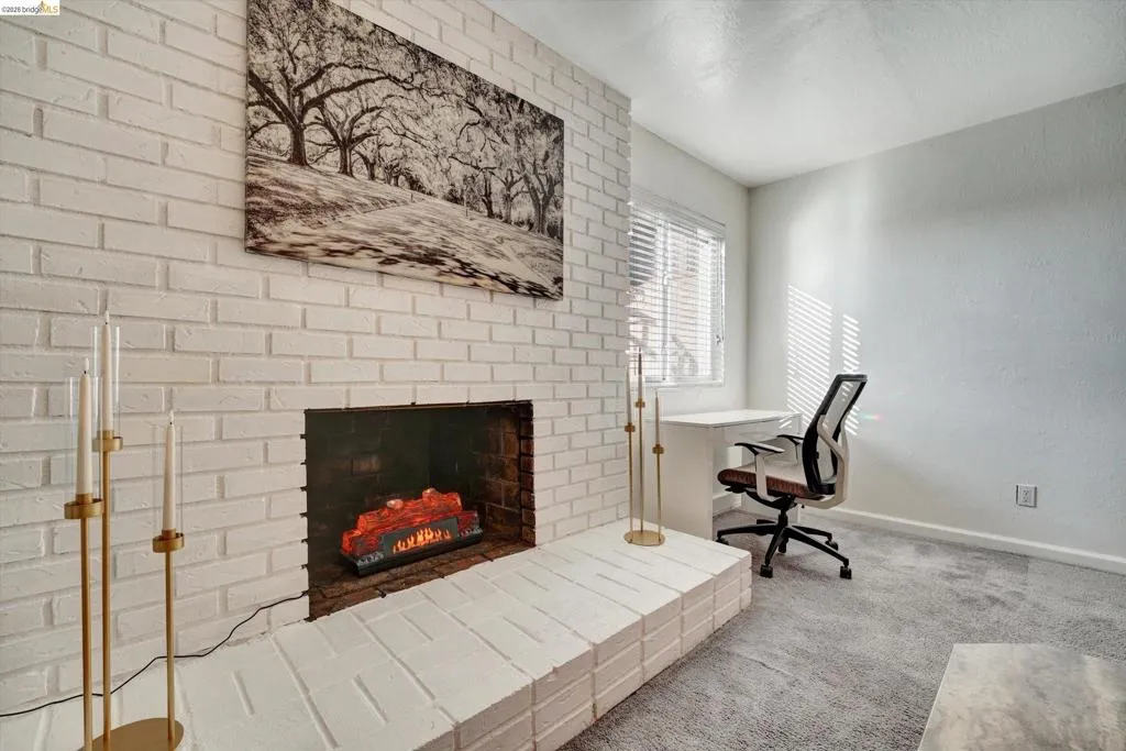 Whitewashed brick fireplace with a raised hearth, light-colored walls, and window with blinds