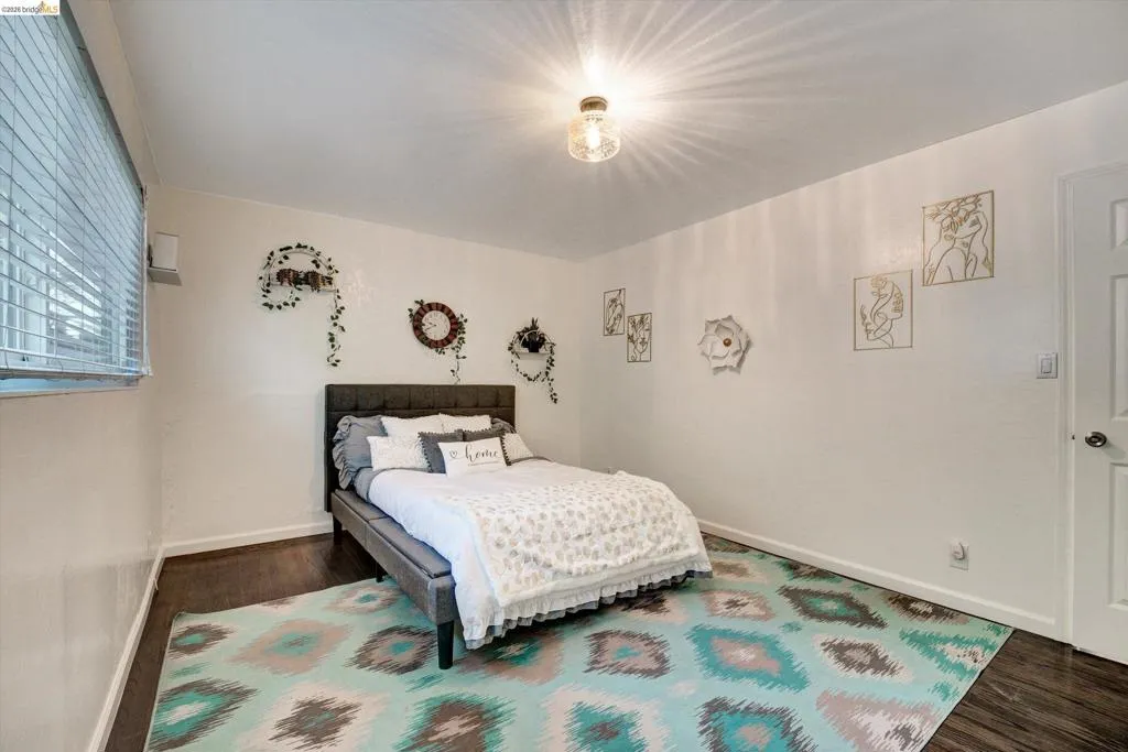 Recessed window with horizontal blinds, wood-finish flooring, white walls, and a ceiling-mounted light fixture